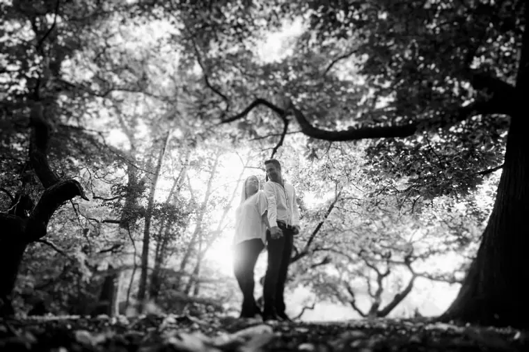 Black-and-white photo of the couple embracing beneath sprawling tree branches