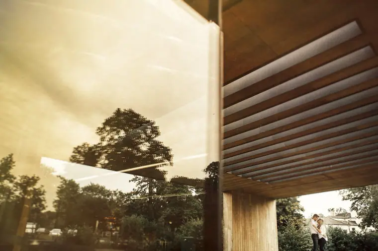 Couple seen in the distance beneath a modern timber canopy in warm light