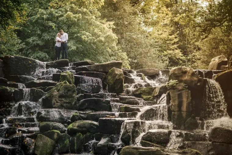 Lauren and Anthony standing above the tumbling rocky waterfall in the woods at Virginia Water