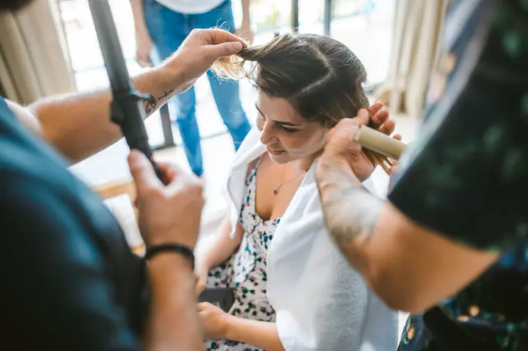 Hairdresser curling the bride's hair as she sits in a floral sundress