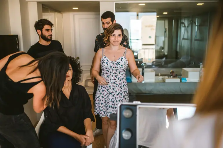 Bride in a floral sundress chatting with her hair and makeup team in a hotel suite