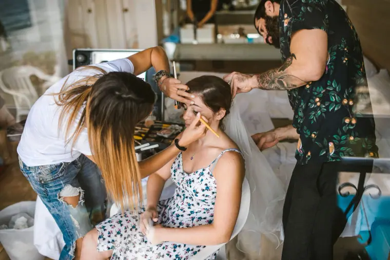 Bride having her makeup and hair done side by side by the stylists