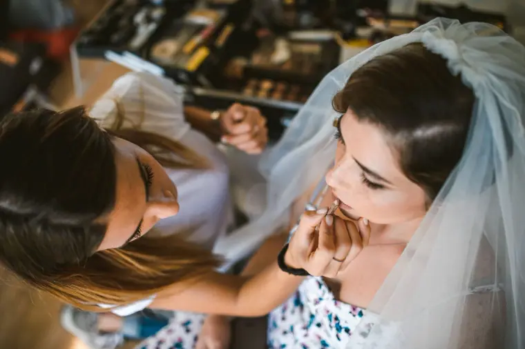 Makeup artist applying lipstick to the bride wearing her veil