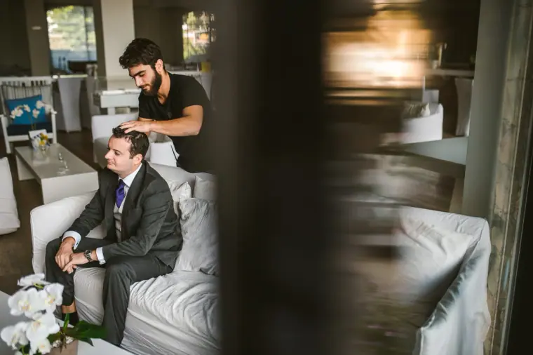 Groom in a grey suit and purple tie relaxing on a white sofa with friends