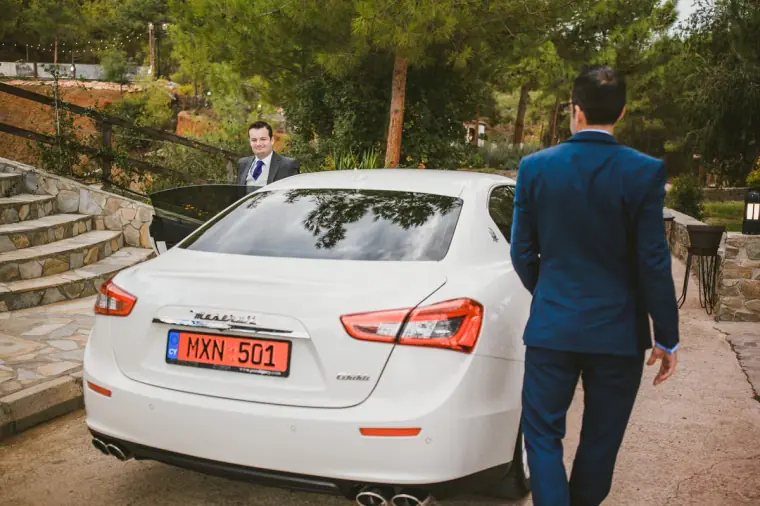 Groom in a navy suit walking up to a white Maserati at the venue
