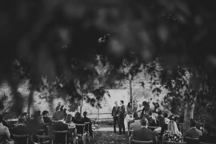 Black-and-white photo of guests gathering for the outdoor ceremony under trees