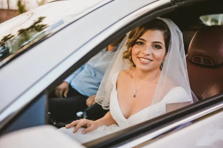 Smiling bride in her veil looking out from the open window of the wedding car