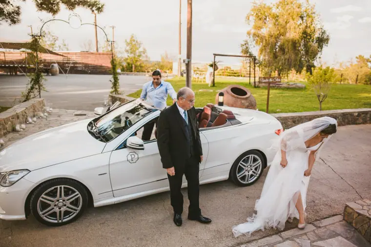 Bride stepping out of a white convertible as her father waits beside it