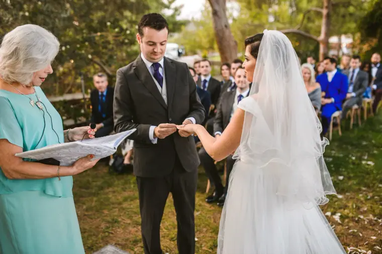 Christopher placing the ring on Nermine's finger as the celebrant looks on