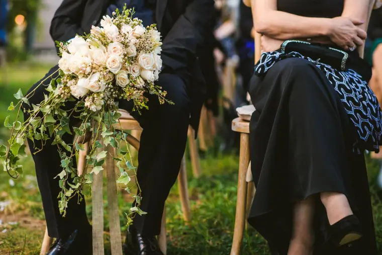 White rose and greenery bouquet resting on a wooden chair among seated guests