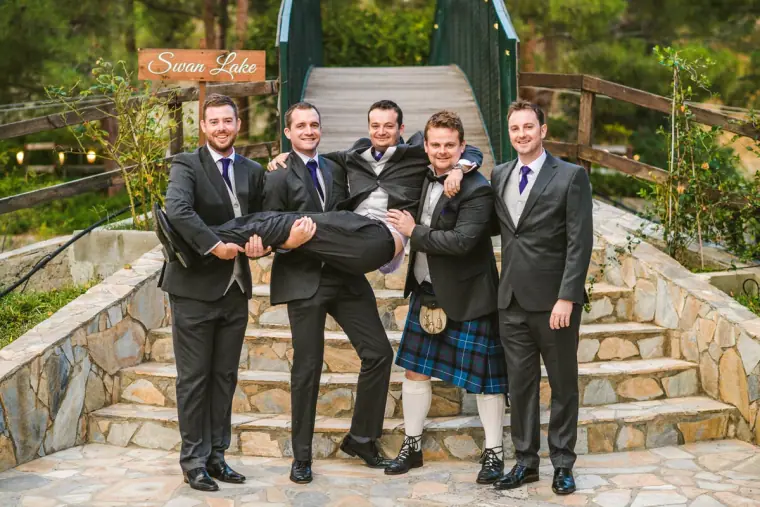 Groomsmen lifting the groom horizontally on stone steps by the Swan Lake sign