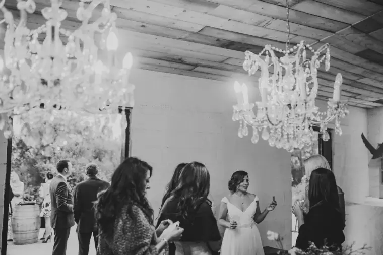 Black-and-white photo of guests mingling under chandeliers with the bride
