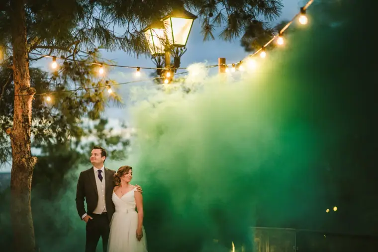 Couple posing as green smoke billows around them beneath festoon lights