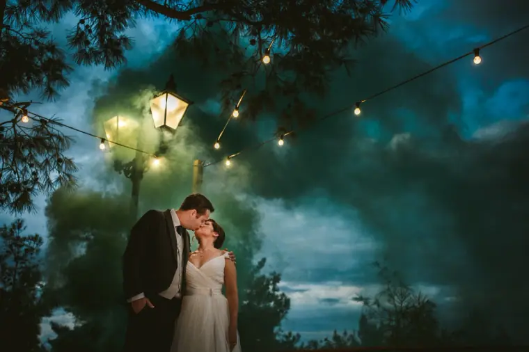 Couple kissing amid swirling green smoke under a lamp post at dusk