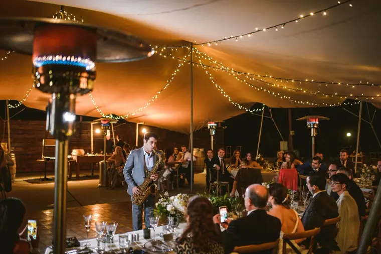 Saxophonist playing among guests dining under the fairy-lit stretch tent