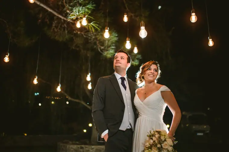 Bride and groom smiling beneath hanging bulbs at night