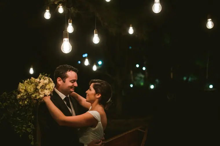 Couple dancing with the bouquet under strings of glowing bulbs