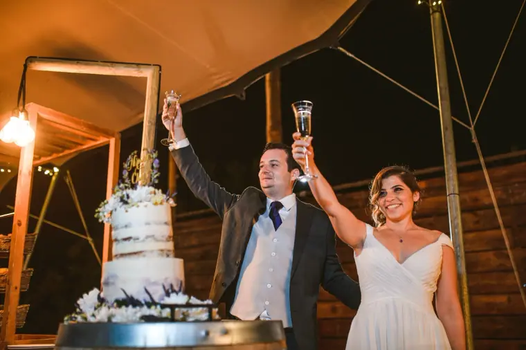 Couple raising glasses of fizz beside the wedding cake