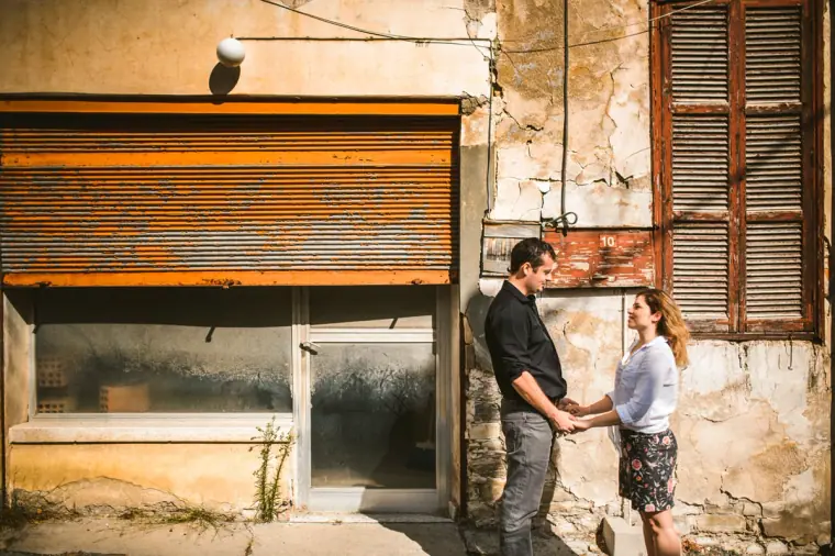 Couple holding hands in front of a weathered shopfront with rusty shutters