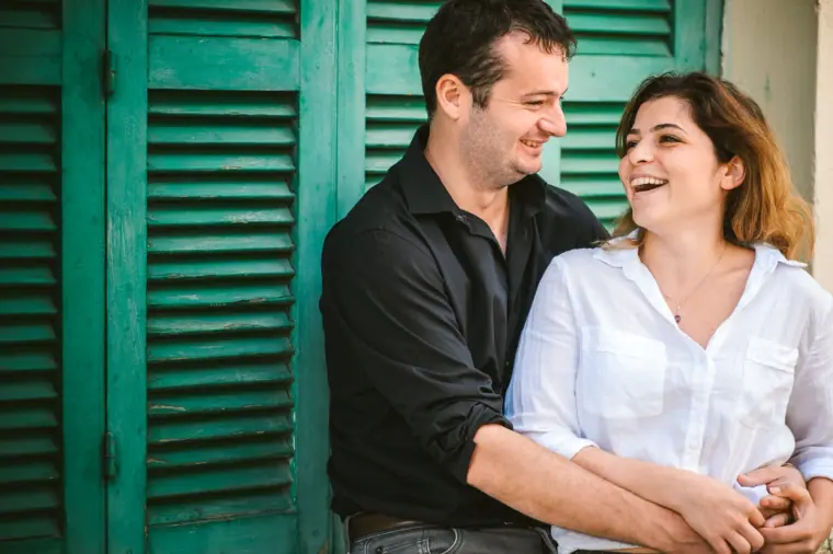 Couple laughing together against bright green wooden shutters