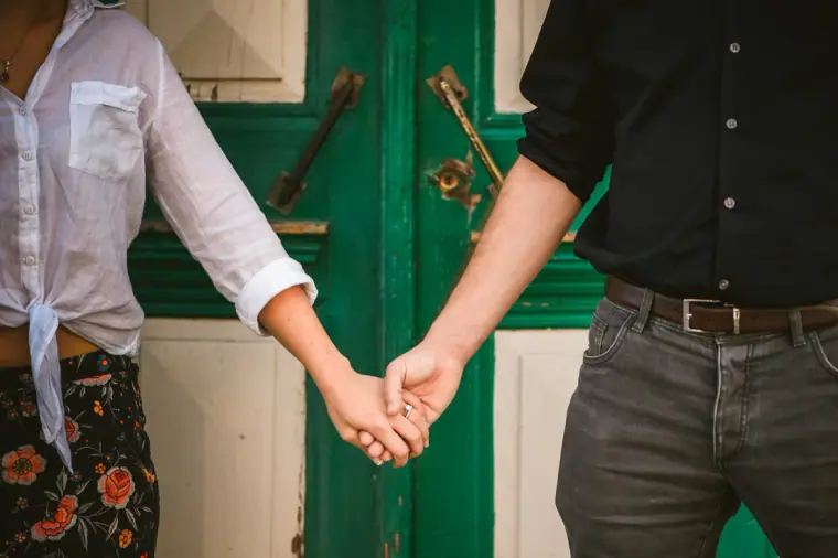 Close-up of the couple holding hands in front of a green door