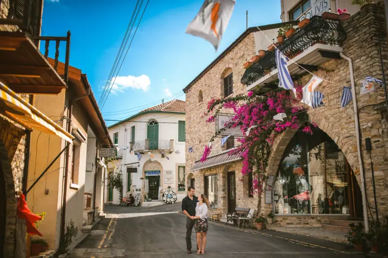 Couple standing small in a sunny street beneath bougainvillea and flags in Lefkara