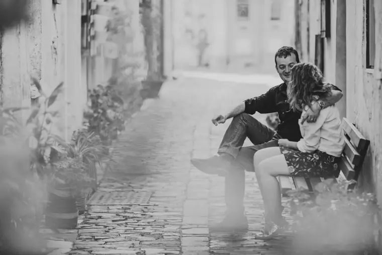 Black-and-white photo of the couple sitting on a bench in a narrow cobbled lane