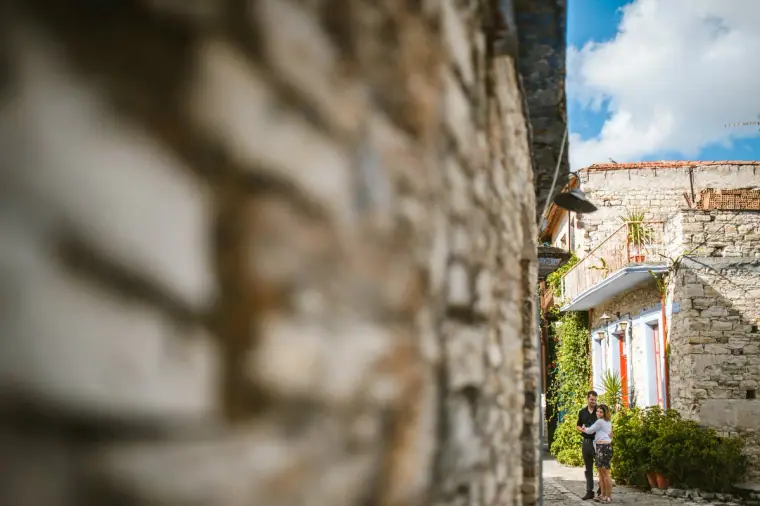 Couple glimpsed down a stone lane past a blurred wall in Lefkara