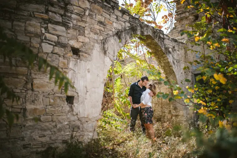 Couple beneath a ruined stone arch overgrown with greenery in Lefkara