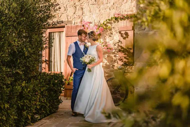 Nicola and Joel holding hands by a stone cottage doorway framed by greenery at Liopetro