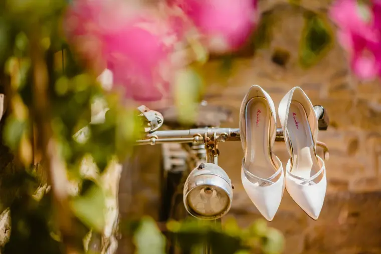Ivory bridal shoes hanging from an old lantern among pink flowers