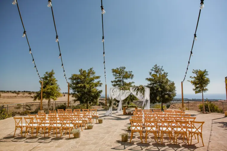 Rows of wooden chairs under festoon lights facing the ceremony arch at Liopetro