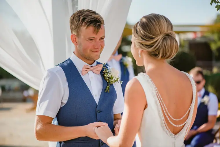 Joel smiling as he holds Nicola's hands, her dress showing a pearl-strand back