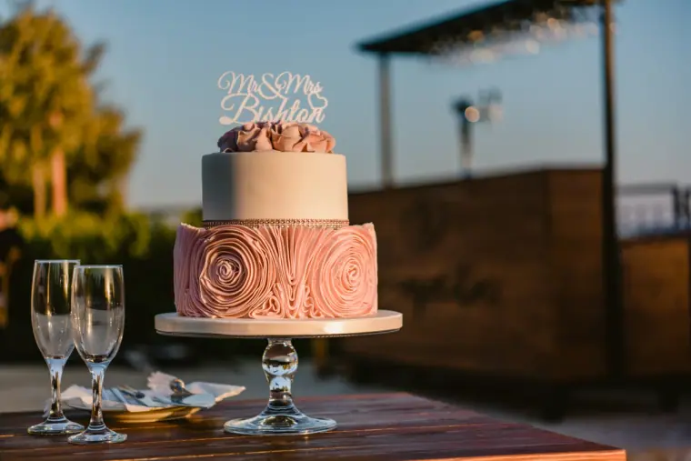 Pink rose-textured wedding cake with a Mr and Mrs topper and champagne flutes