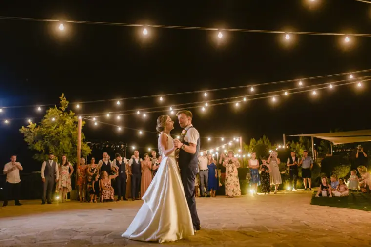 Couple dancing under festoon lights as guests watch around the terrace