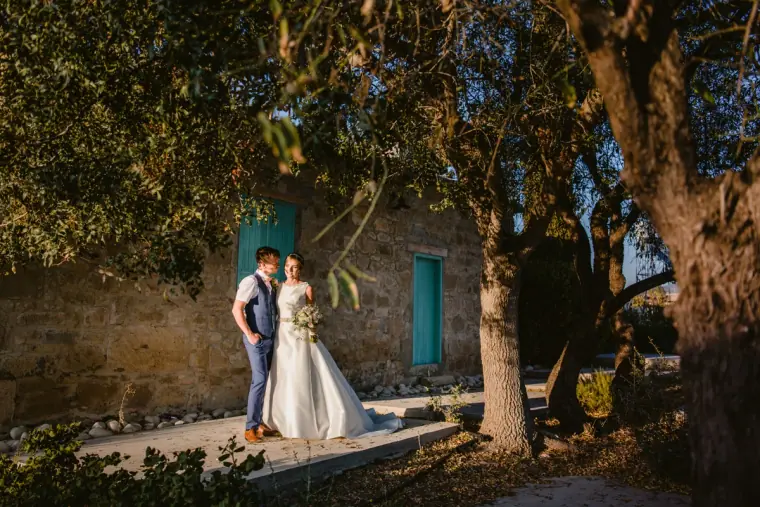 Couple standing by a stone house with turquoise shutters under olive trees
