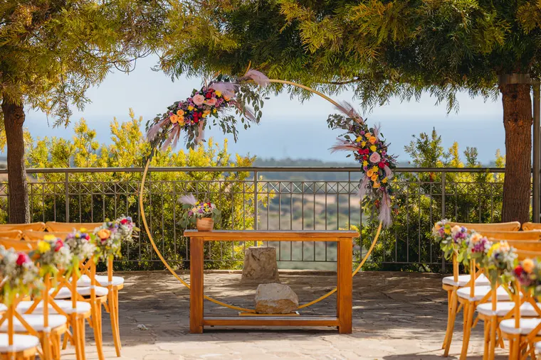 Circular floral ceremony arch and wooden chairs overlooking the coast at Liopetro, Kouklia