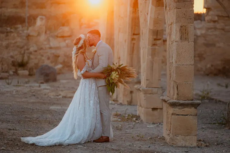Couple kissing among ancient stone columns in warm sunset light, Kouklia