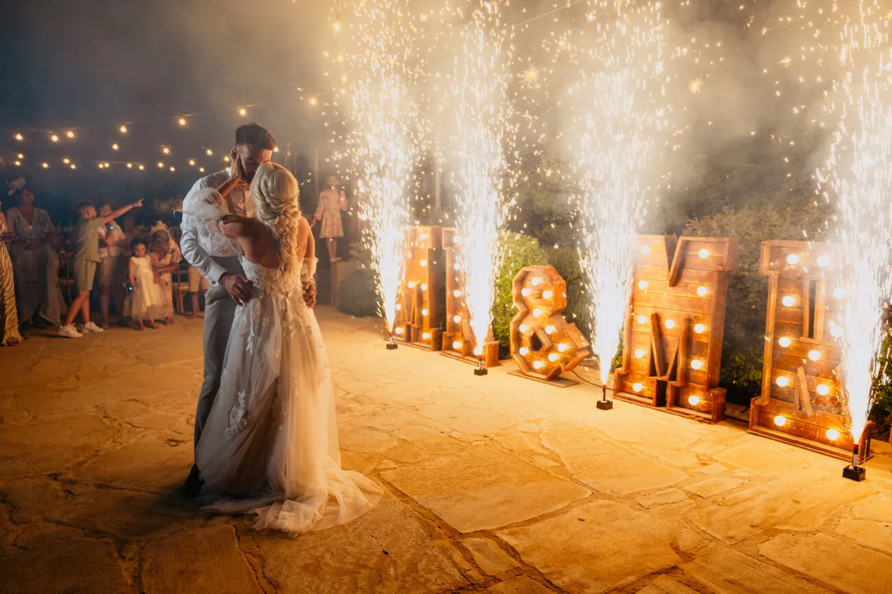 Couple embracing beside cold-spark fountains and illuminated M&M letters at Liopetro
