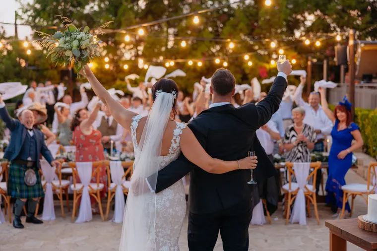 Guests cheering and waving napkins as the couple raise their arms at the evening reception