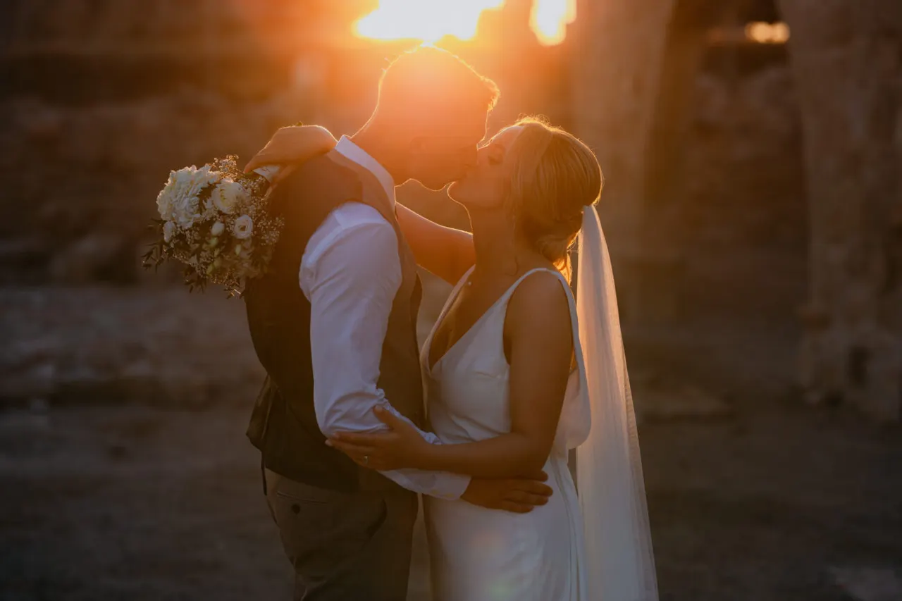 Couple kissing in silhouette, backlit by the setting sun between stone pillars