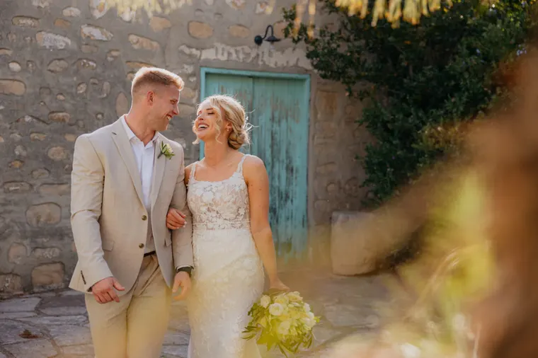 Bride and groom smiling beside a teal door in a stone courtyard at Liopetro, Kouklia