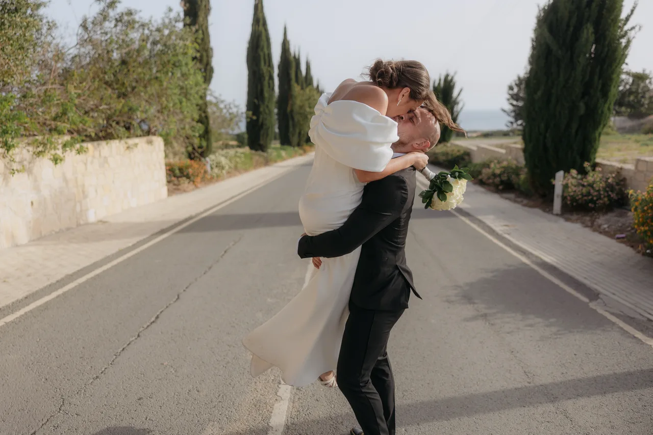 Groom lifting the bride for a kiss in the middle of a cypress-lined road near Kouklia