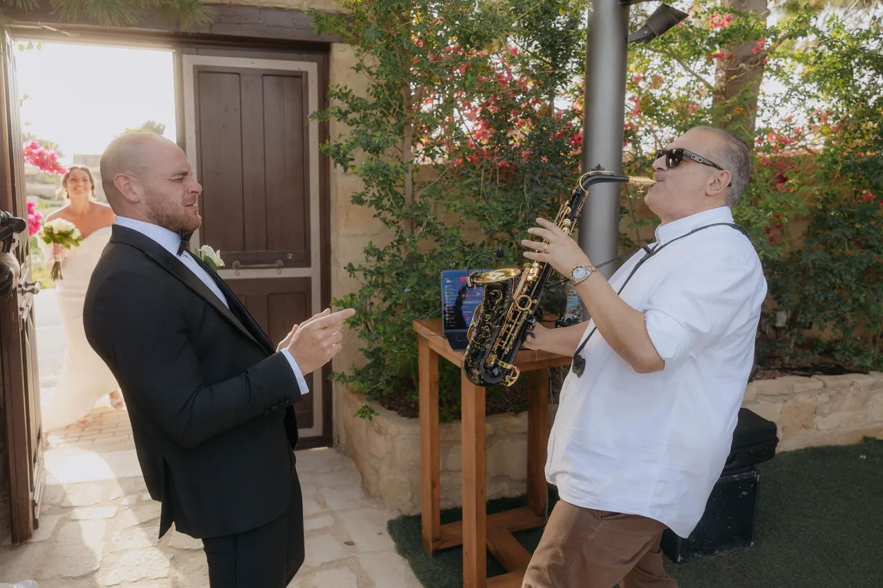 Groom laughing with a saxophonist playing at the reception at Liopetro, Kouklia