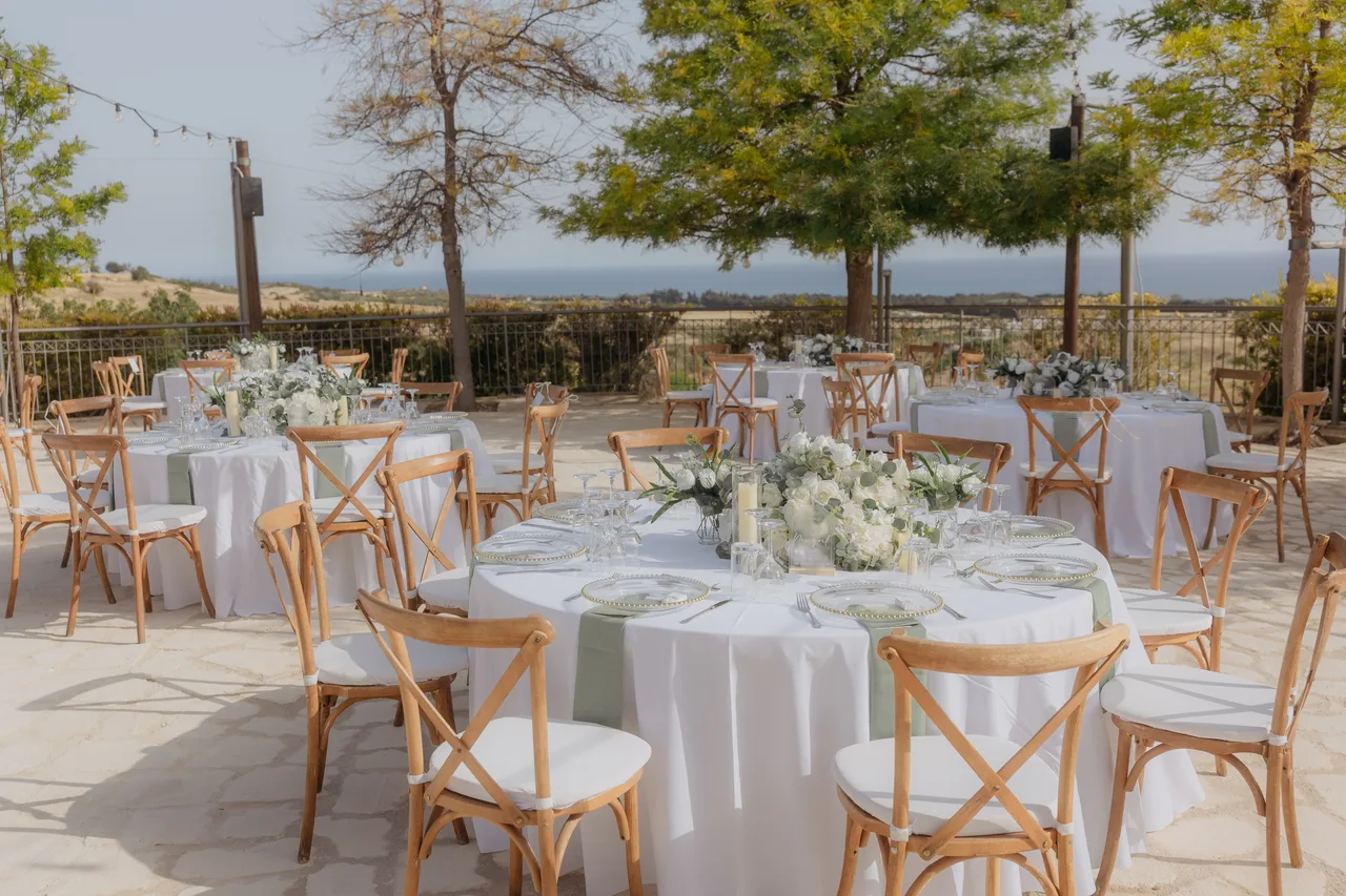 Round reception tables with white flowers set on the terrace overlooking the coast at Liopetro