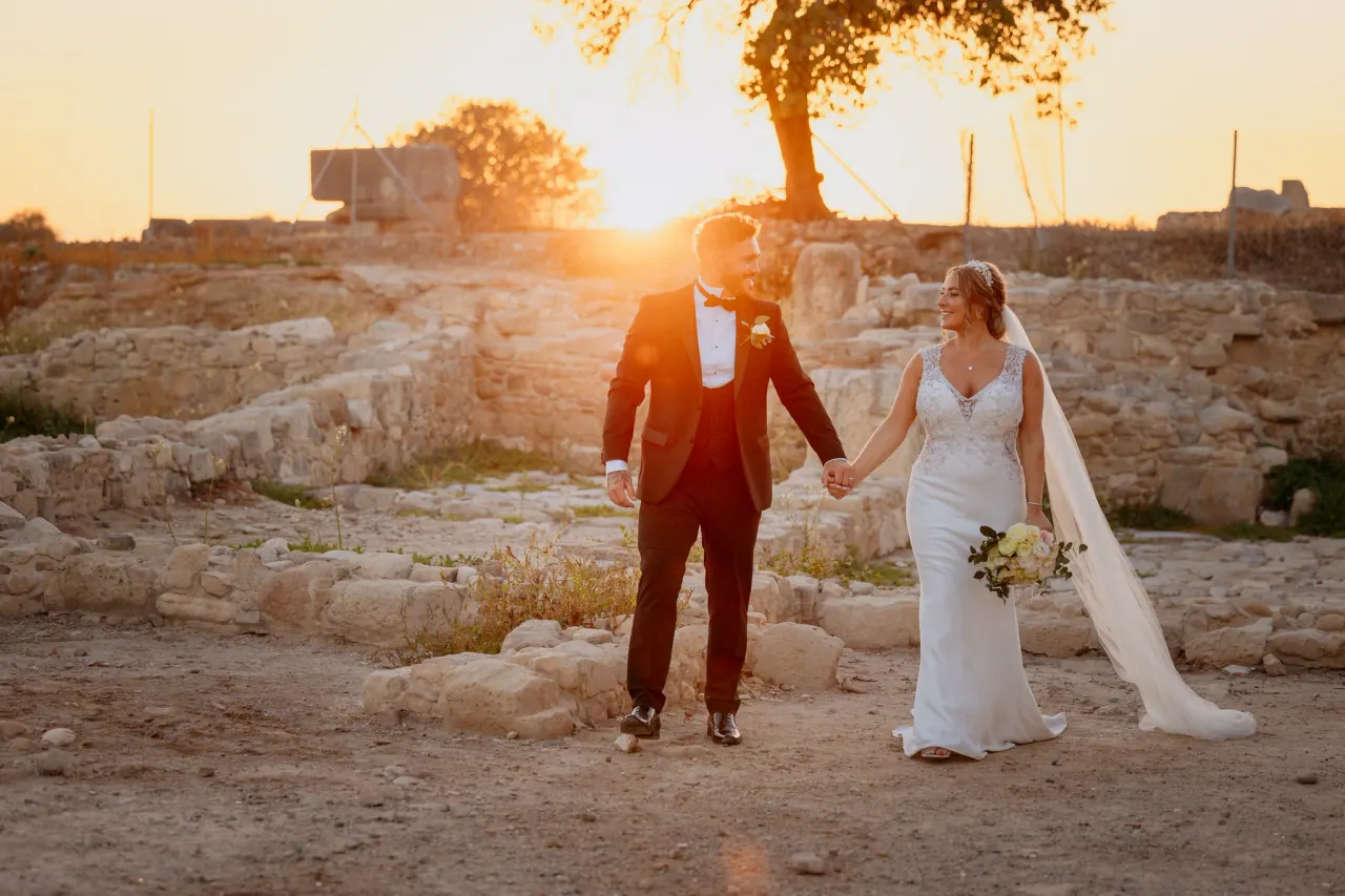 Bride and groom walking hand in hand through ancient ruins at sunset near Liopetro, Kouklia