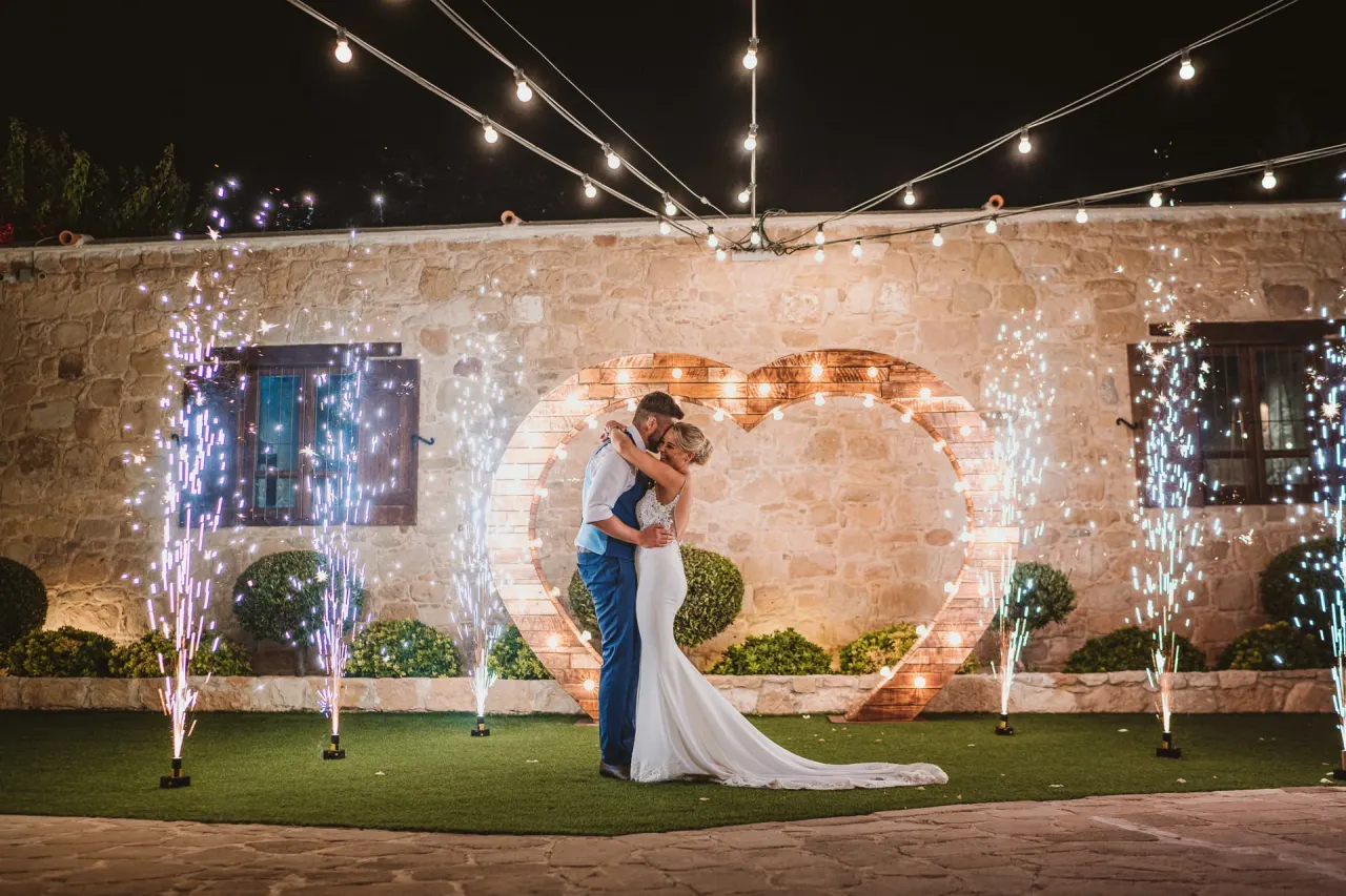 Natalie and Jack kissing by a light-up heart as cold sparklers fire on the lawn at Liopetro, Kouklia
