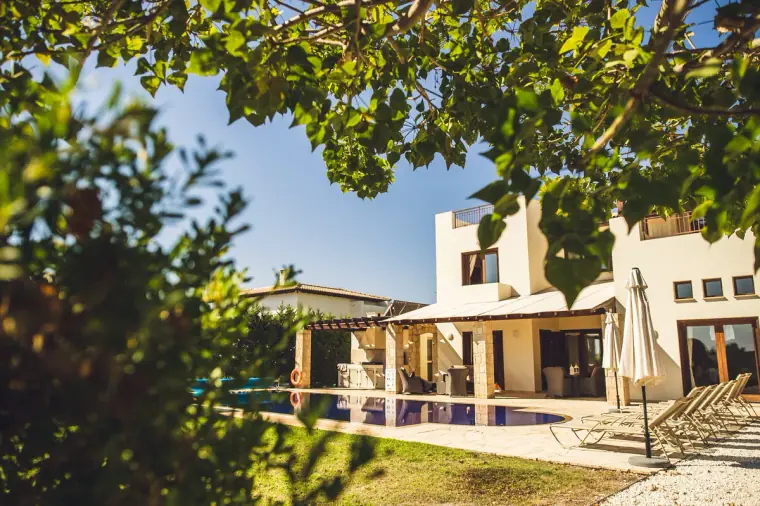 Villa and swimming pool seen through leafy branches on a sunny day at Liopetro, Kouklia