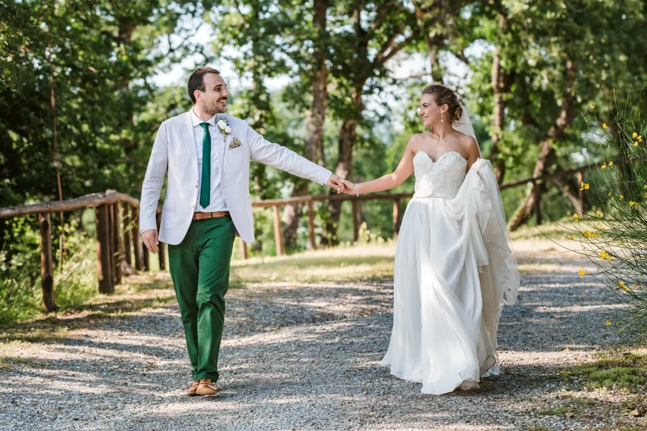 Jess and Dan walking hand in hand along a tree-lined gravel path at Livernano Estate, Tuscany