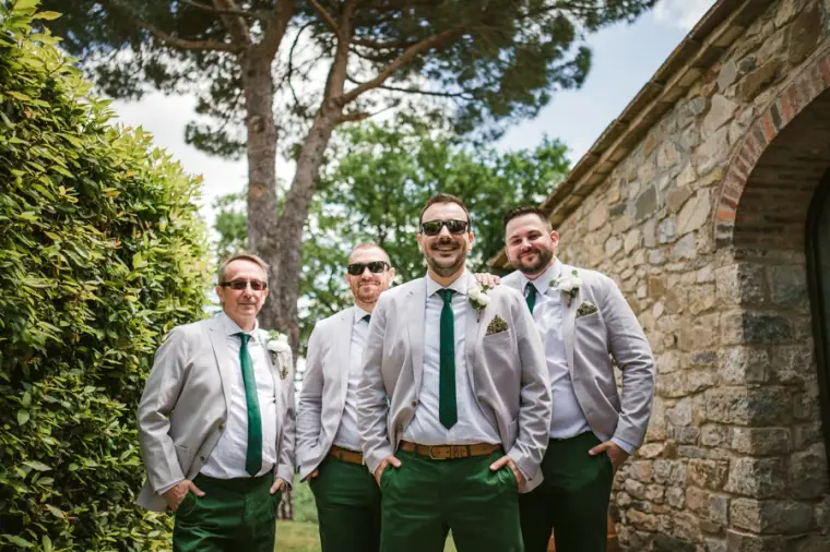 Groom and groomsmen in grey jackets and green trousers by a stone arch at Livernano Estate